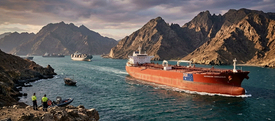 "ناقلة نفط تحمل العلم الأسترالي تبحر في مضيق هرمز وسط تضاريس جبلية، ترمز لجهود تأمين سيادة الوقود الأسترالي وحمايته من النزاعات الدولية."