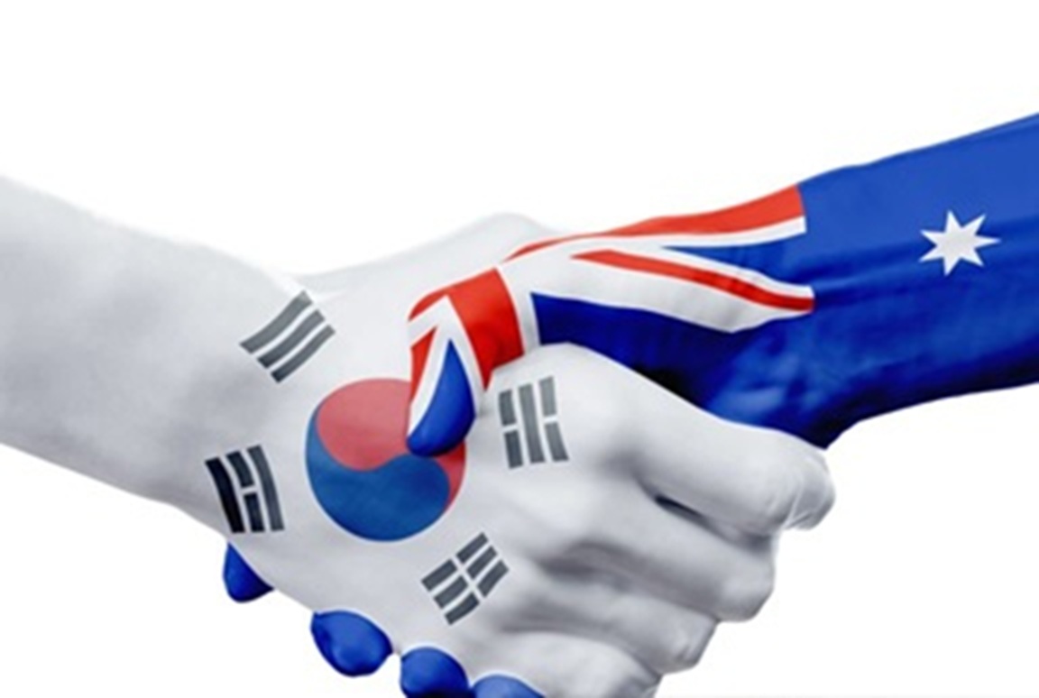 صورة قريبة (ماكرو) ليدي شخصين تصافحان بقوة؛ اليد اليسرى مطلية بعلم كوريا الجنوبية (الأبيض مع التايغوك الأزرق والأحمر)، واليد اليمنى مطلية بعلم أستراليا (الأزرق مع نجوم الصليب الجنوبي واتحاد المملكة المتحدة)، على خلفية بيضاء.