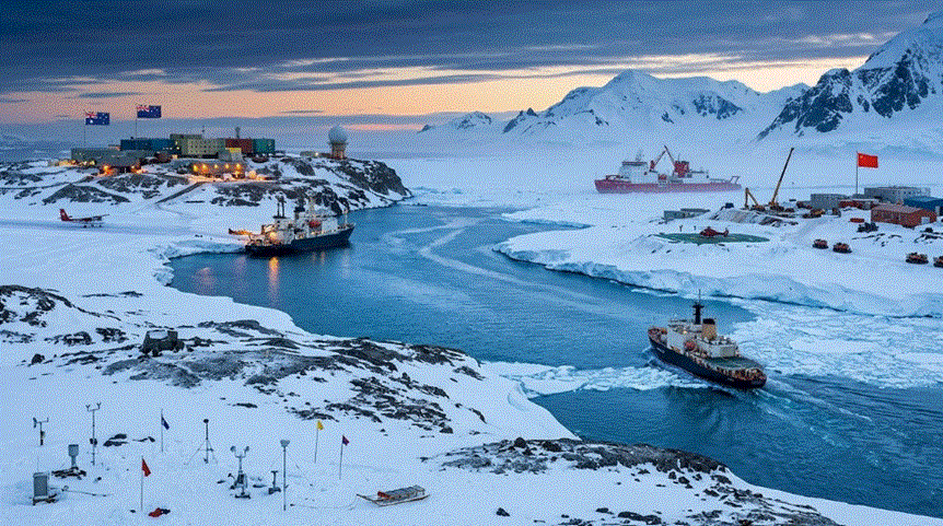 منظر بانورامي جوي لمحطات بحثية وسفن في القارة القطبية الجنوبية عند الغسق. تظهر على اليسار محطة مرفوع عليها علمان لأستراليا ونيوزيلندا، وعلى اليمين سفن ومنشآت مرفوع عليها علم الصين، مع سفينة ثالثة تبحر في ممر مائي بينهما، وسط جبال مغطاة بالثلوج.