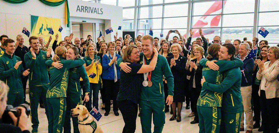 "لقطة أفقية نابضة بالحياة لاستقبال بعثة أستراليا البارالمبية الشتوية في مطار سيدني. يظهر في المقدمة البطل بن تودهوب مبتسماً ويحمل ميدالياته وهو يعانق سيدة، بينما يعانق رياضيون آخرون بالزي الأخضر والذهبي عائلاتهم. الحشد يلوح بالأعلام الأسترالية، ويوجد كلب خدمة جالس، وطائرة كانتاس تظهر عبر النافذة في الخلفية تحت شعار 'Arrivals'."