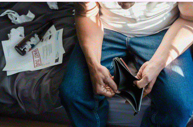 رجل يجلس ممسكاً بمحفظة فارغة بينما تظهر فواتير متأخرة بجانبه، في إشارة إلى الضغوط المالية.