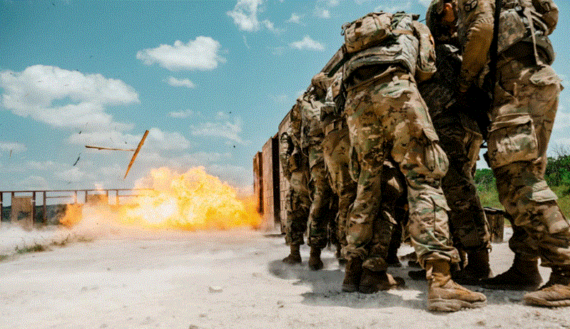 جنود يشاركون في تدريبات عسكرية بالذخيرة الحية خلال مناورات مشتركة، مع انفجار في الخلفية يحاكي ظروف القتال الواقعي.