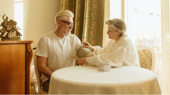 زوجان مسنان يجلسان في المنزل بينما تقوم الزوجة بقياس ضغط الدم لزوجها، في مشهد يعكس الاهتمام بالصحة لدى كبار السن.