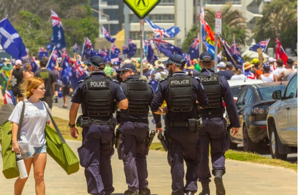 عناصر من الشرطة الأسترالية يسيرون أمام حشد من المتظاهرين الذين يرفعون أعلام أستراليا خلال تجمع سياسي في الشارع.