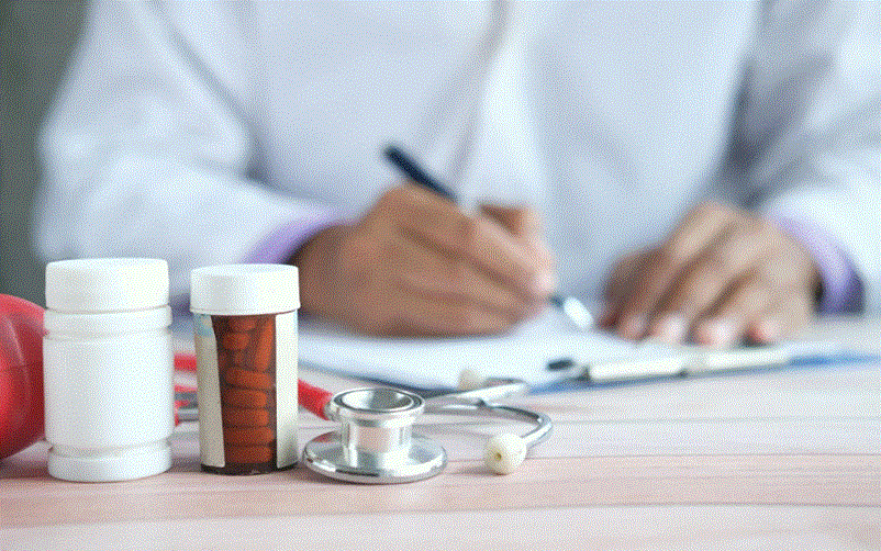 طبيب يكتب ملاحظات طبية بجانب أدوات طبية وأدوية على مكتب