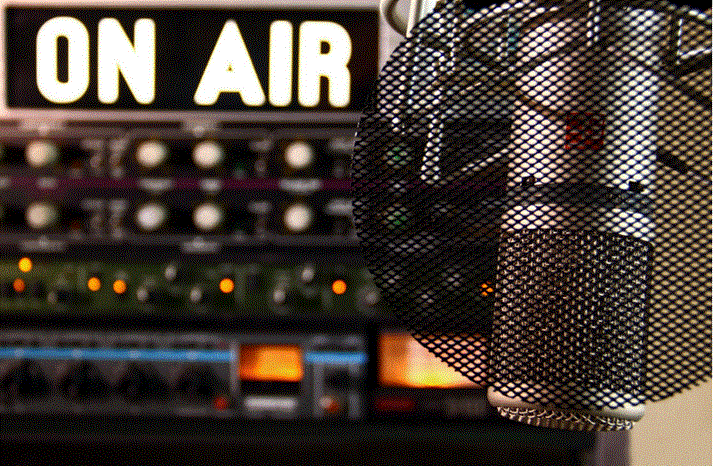 ميكروفون داخل استوديو إذاعي مع لافتة “On Air” مضيئة في الخلفية أثناء البث