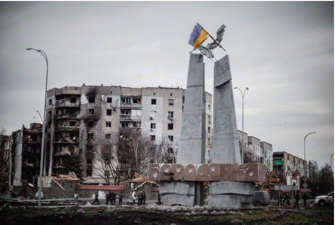 نصب تذكاري يحمل العلم الأوكراني وسط مدينة متضررة من الحرب مع مبانٍ مدمرة في الخلفية