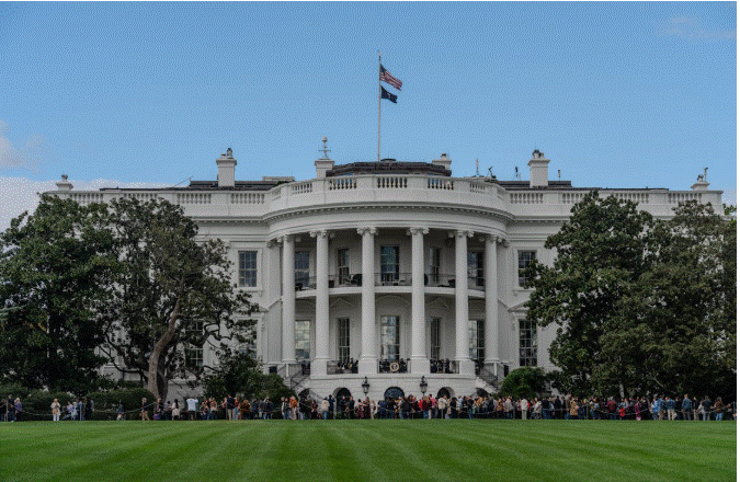 مبنى البيت الأبيض في واشنطن مع تجمع أشخاص في الساحة الأمامية وسط إجراءات أمنية مشددة.