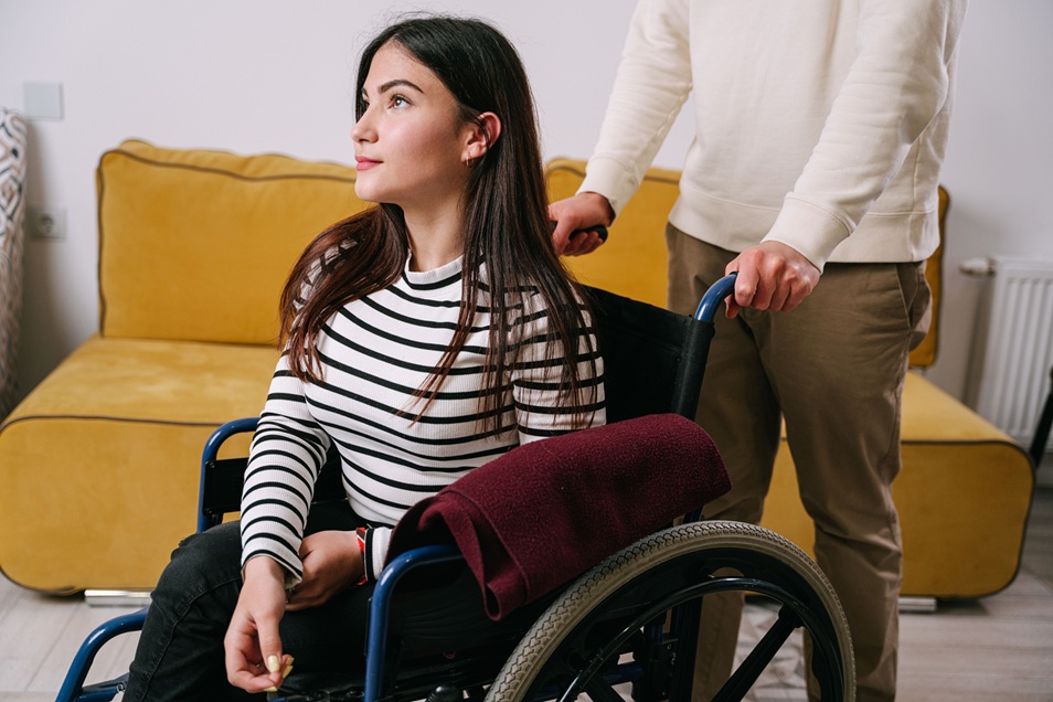 امرأة تستخدم كرسياً متحركاً تتلقى المساعدة من مقدم رعاية داخل منزل، في صورة تعبر عن خدمات الدعم للأشخاص ذوي الإعاقة وبرنامج NDIS في أستراليا.