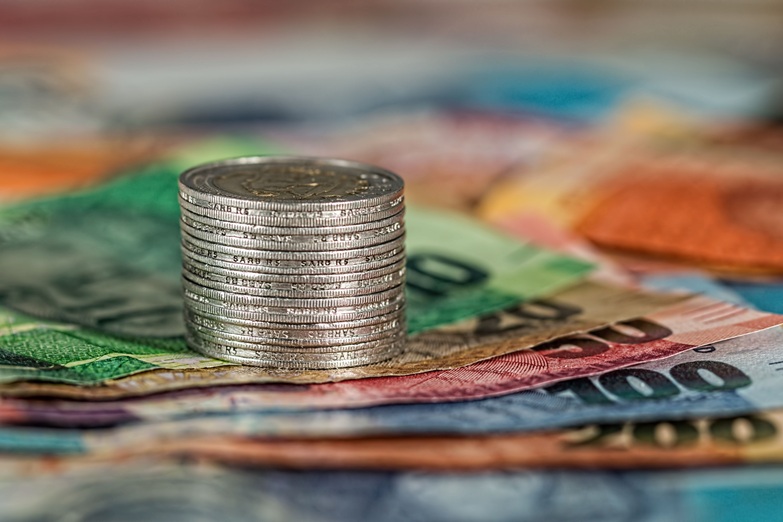 كومة من العملات المعدنية فوق أوراق نقدية ملونة، ترمز إلى التحديات الاقتصادية في أستراليا وارتفاع الديون الحكومية والحاجة إلى إصلاحات مالية وضريبية.