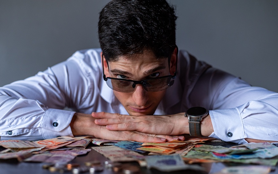 رجل ينظر بقلق إلى أوراق نقدية تعبيراً عن تأثير ارتفاع أسعار الفائدة وتكاليف المعيشة.
