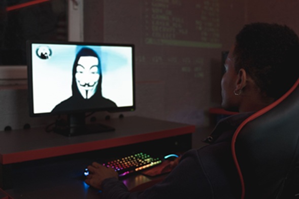 شخص أمام شاشة كمبيوتر تعرض رمزاً لقراصنة الإنترنت في مشهد يعبر عن الهجمات الإلكترونية والأمن السيبراني.