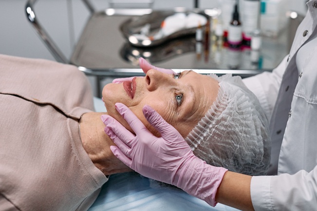 سيدة تستلقي داخل عيادة تجميل بينما تفحص أخصائية وجهها، في صورة تعكس أهمية الاستشارة الطبية والسلامة قبل إجراء جراحات التجميل.